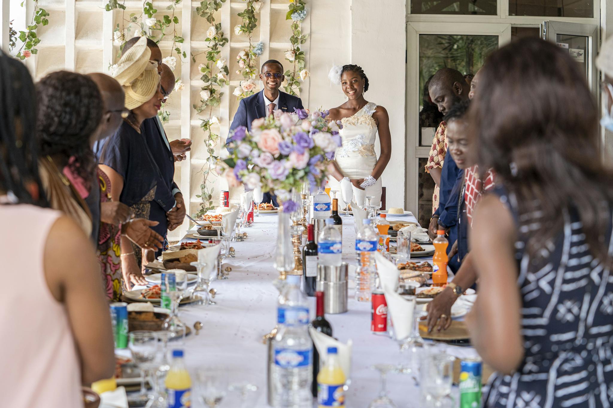 A joyful couple at their wedding reception surrounded by guests enjoying a meal.